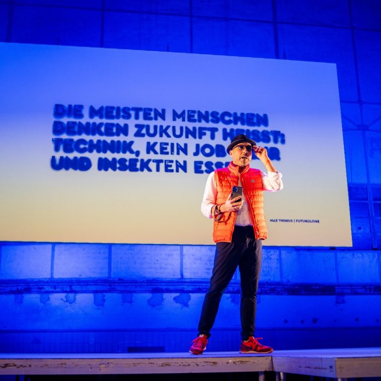 Ein Redner steht auf einer Bühne vor einer Folie mit einem Zitat über Technologie und Zukunft.
