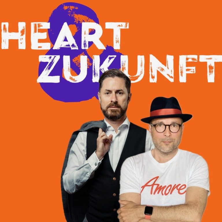 Zwei Männer posieren vor orangefarbigem Hintergrund mit Aufschrift „Heart & Zukunft“.
