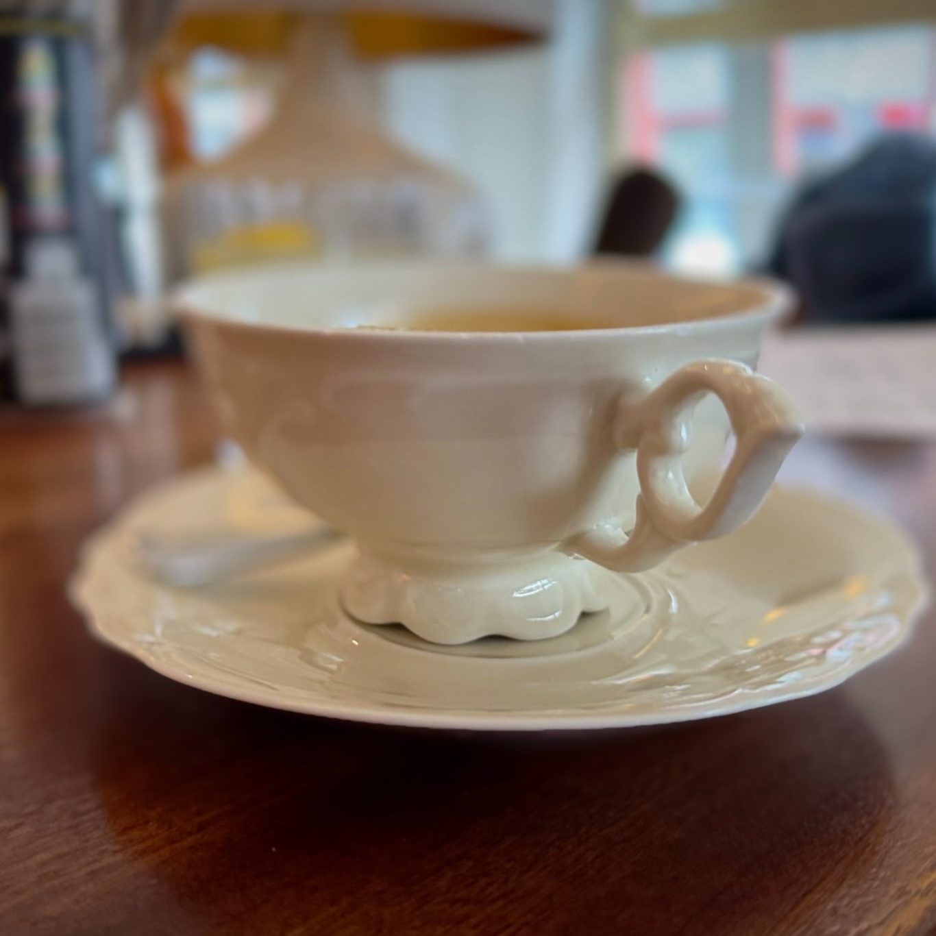 Weiße Teetasse mit Untertasse auf einem Holztisch, neben einem Löffel.