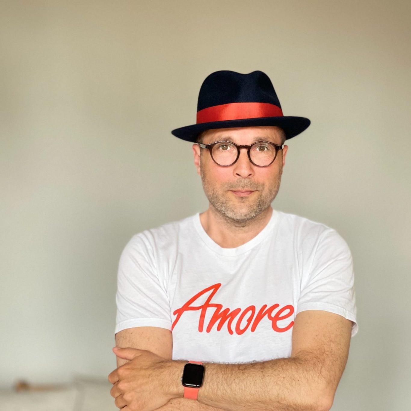 Mann mit Brille in T-Shirt mit "Amore" und schwarzem Hut mit rotem Band.